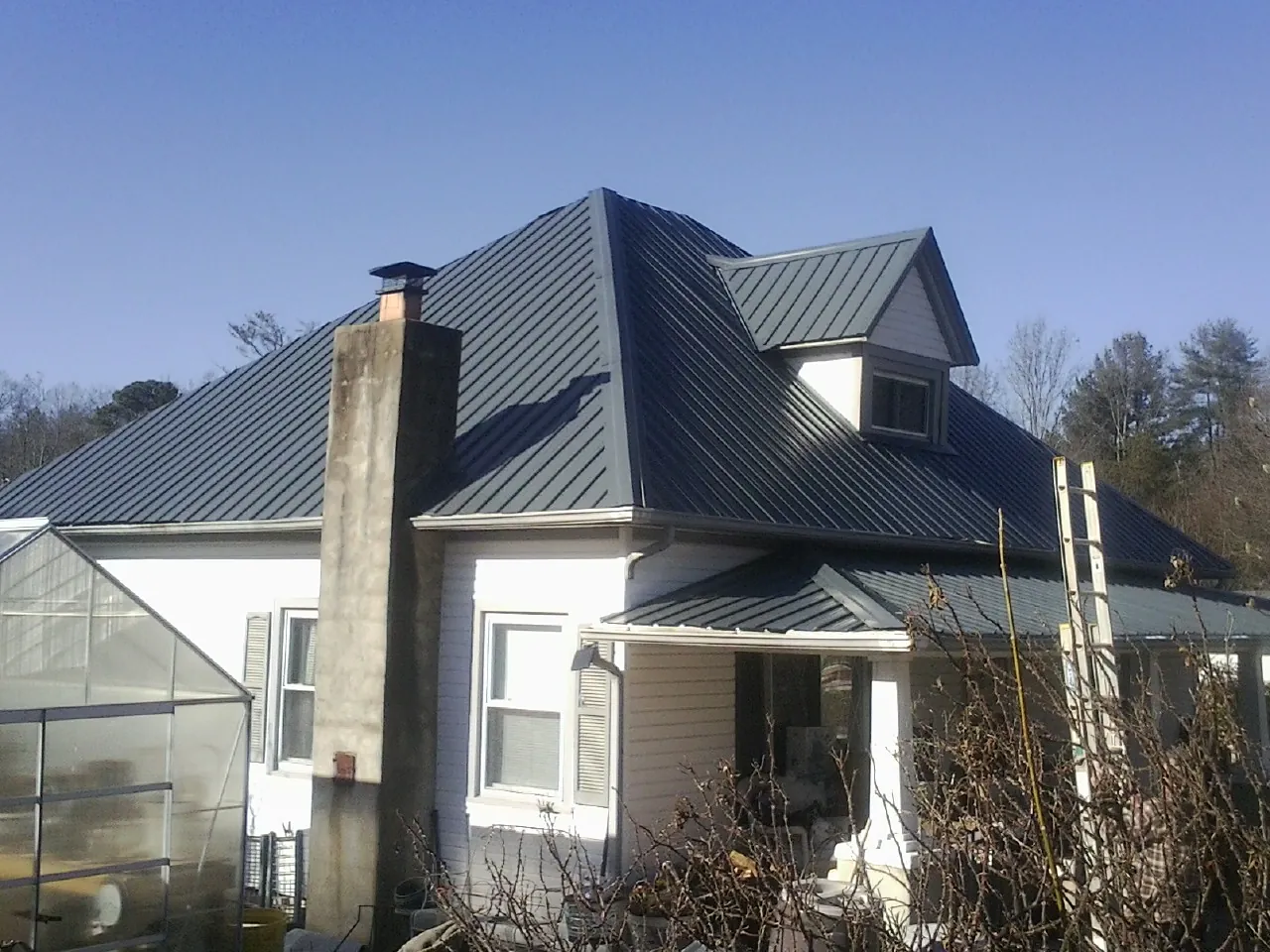 Dark blue standing seam metal roof on a white farmhouse with dormer — Slate & Tile Roof Repair by Roofing Brothers in Round O