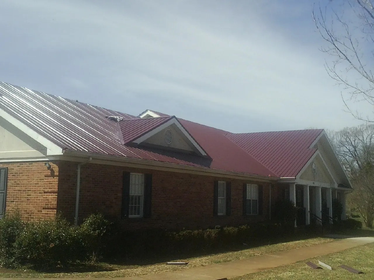 Red metal roof with gabled entries on a long brick building, from a Hail Damage Roof Repair job in Round O