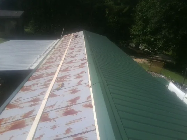 Old rusted panels beside newly installed green metal roofing — Wind Damage Roof Repair by Roofing Brothers in Round O