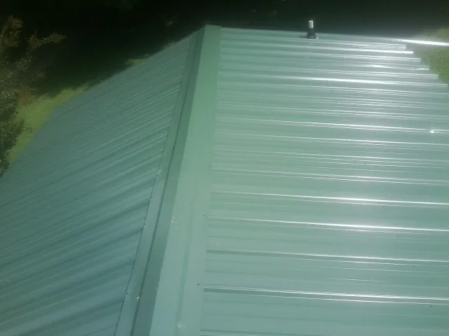 New green metal panels meeting at the ridge of a roof — Flat Roof Repair work by our crew in Round O