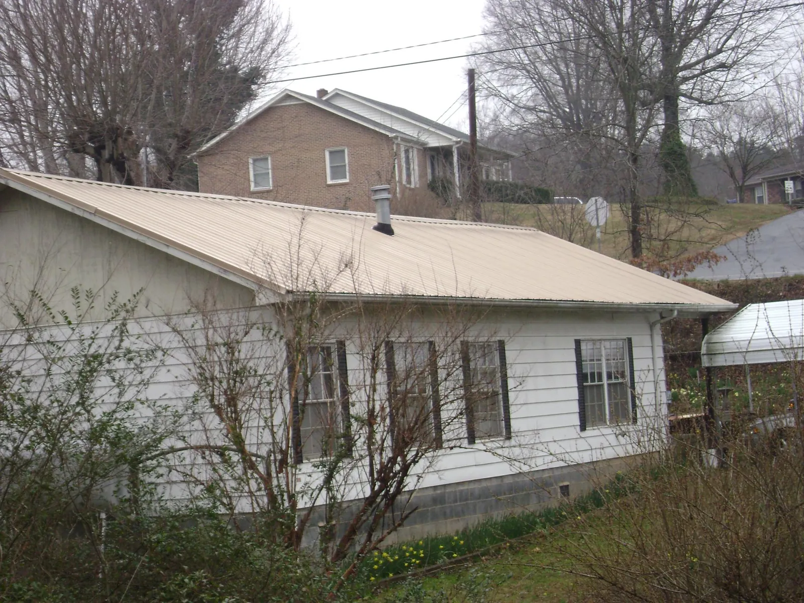 Tan metal roof on a white sided house set into a hillside — Commercial Roofing by Roofing Brothers in Round O