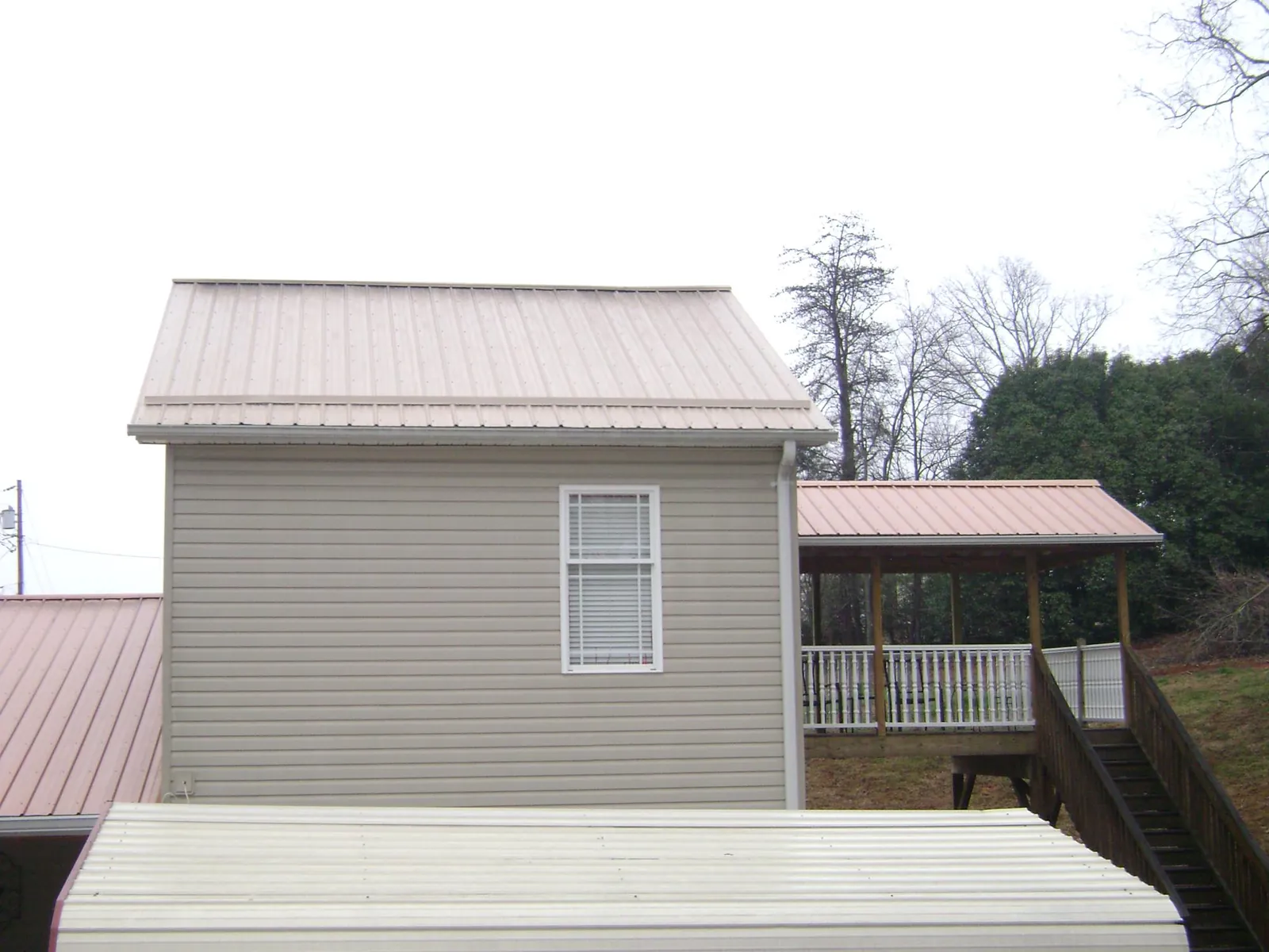 Tan metal roofs on a two story addition and attached porch, from a Roof Replacement job in Round O